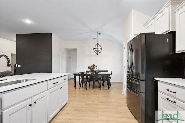 kitchen with black fridge, sink, decorative light fixtures, light hardwood / wood-style flooring, and white cabinetry