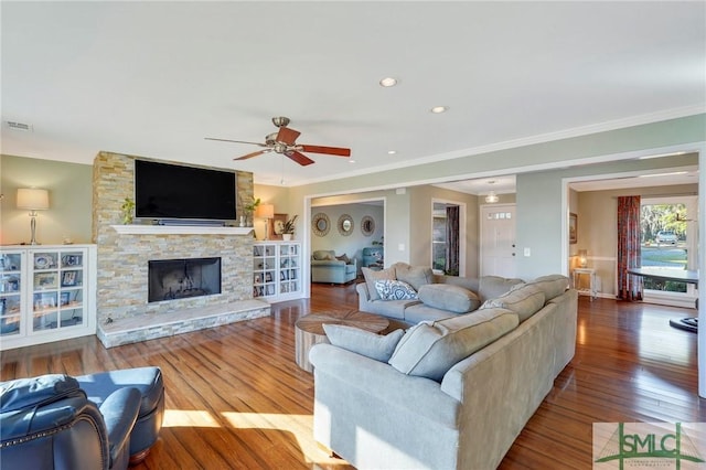 living room with hardwood / wood-style flooring, a stone fireplace, ceiling fan, and ornamental molding