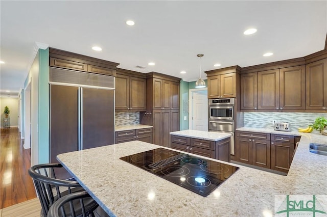 kitchen with light stone counters, black electric stovetop, oven, and decorative light fixtures