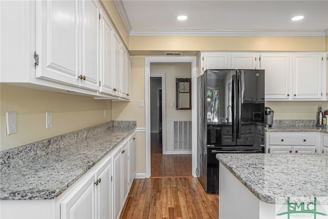 kitchen featuring light wood-type flooring, black fridge, light stone counters, crown molding, and white cabinetry