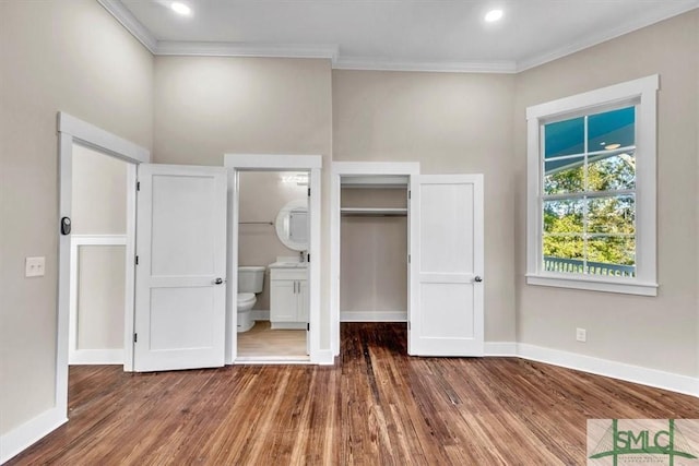 unfurnished bedroom featuring a walk in closet, ensuite bath, ornamental molding, dark wood-type flooring, and a closet