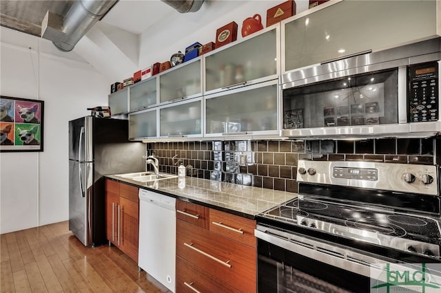 kitchen featuring stainless steel appliances, light hardwood / wood-style floors, sink, backsplash, and light stone counters