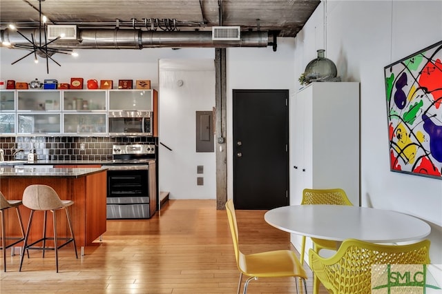 kitchen with appliances with stainless steel finishes, decorative backsplash, a notable chandelier, light wood-type flooring, and electric panel