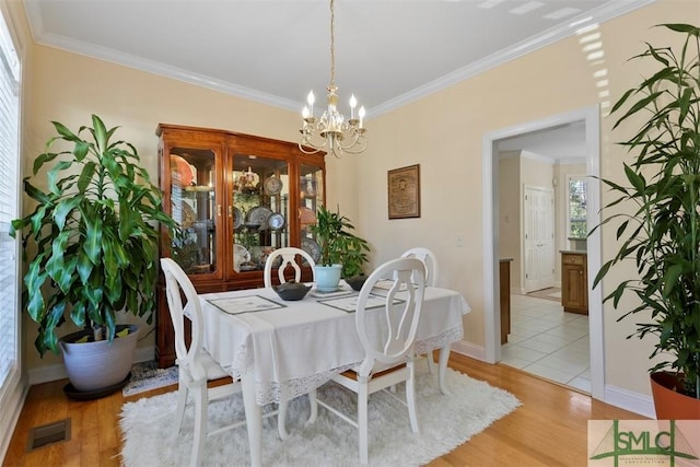 dining space featuring light hardwood / wood-style floors, crown molding, and a notable chandelier