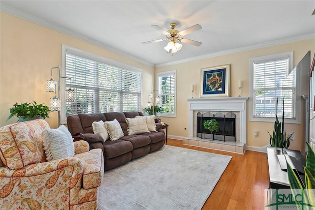 living room with a tiled fireplace, crown molding, light hardwood / wood-style floors, and a healthy amount of sunlight