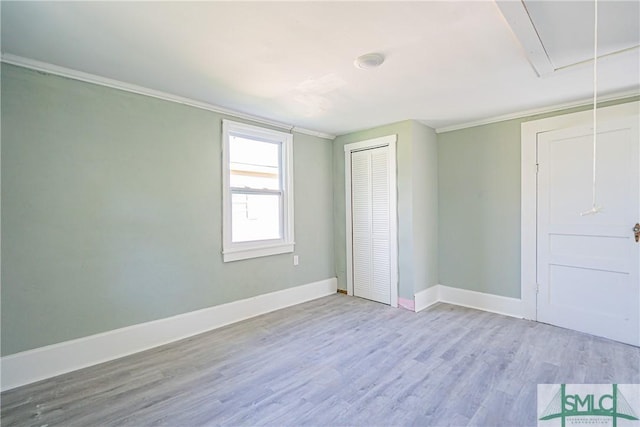 unfurnished bedroom featuring a closet, baseboards, crown molding, attic access, and wood finished floors
