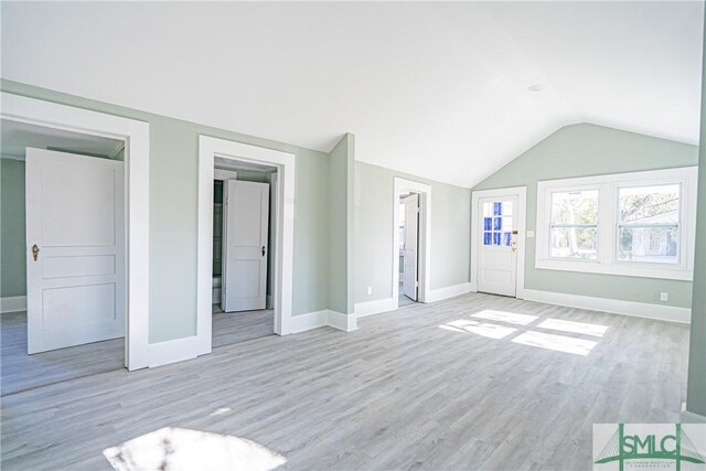 unfurnished living room featuring light wood-type flooring, baseboards, and vaulted ceiling