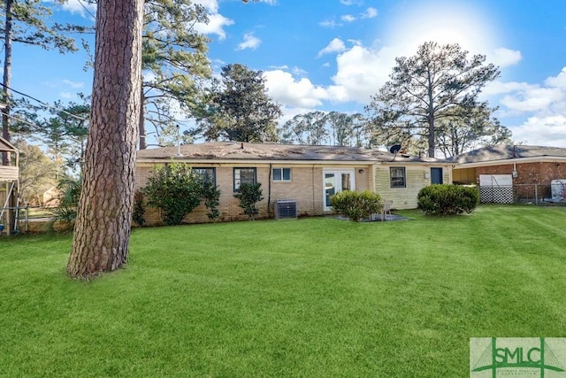 rear view of house featuring a yard, brick siding, central AC, and fence