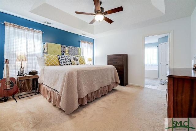 carpeted bedroom with a tray ceiling, ceiling fan, and ensuite bathroom