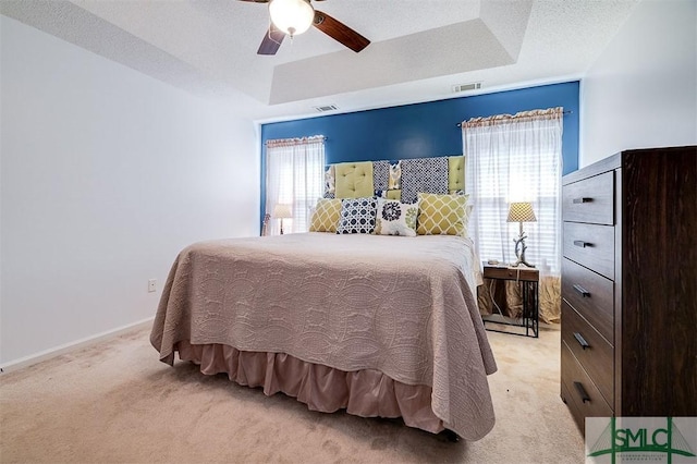 carpeted bedroom featuring a tray ceiling, multiple windows, ceiling fan, and a textured ceiling