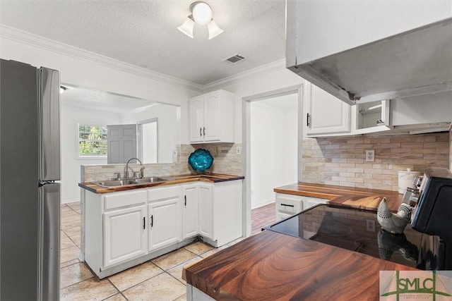 kitchen with butcher block counters, extractor fan, sink, white cabinetry, and stainless steel refrigerator