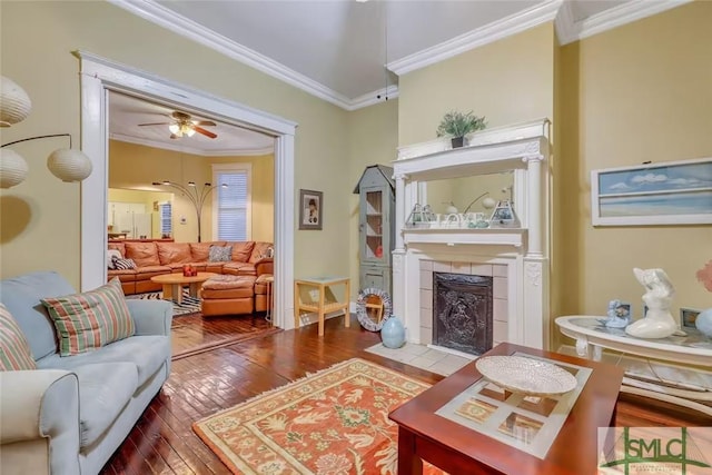 living room with a tile fireplace, ceiling fan, wood-type flooring, and ornamental molding