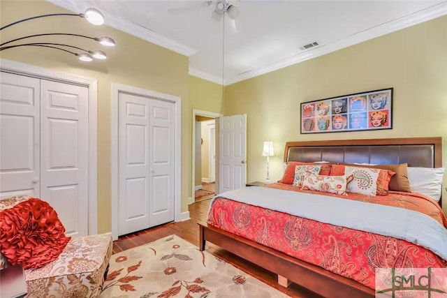 bedroom featuring light wood-type flooring, two closets, ceiling fan, and crown molding