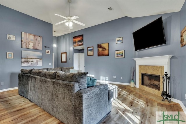 living room with ceiling fan, vaulted ceiling, light hardwood / wood-style flooring, and a tiled fireplace