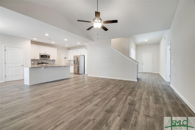 unfurnished living room with ceiling fan, vaulted ceiling, and light wood-type flooring