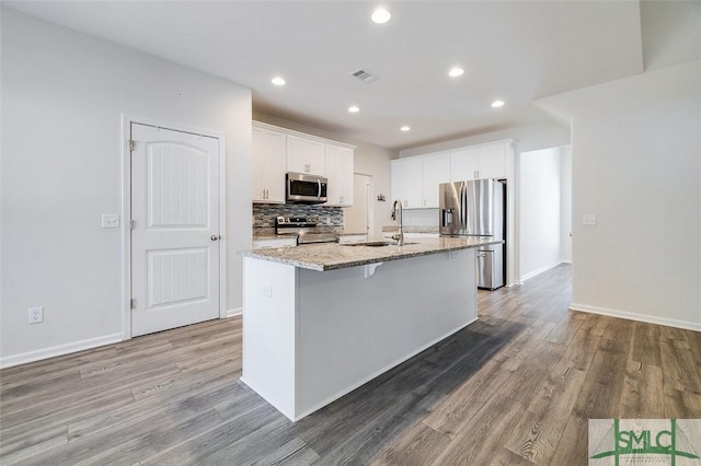 kitchen with white cabinetry, sink, stainless steel appliances, light stone counters, and an island with sink