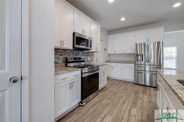 kitchen with white cabinets, stainless steel appliances, light stone counters, and light hardwood / wood-style floors