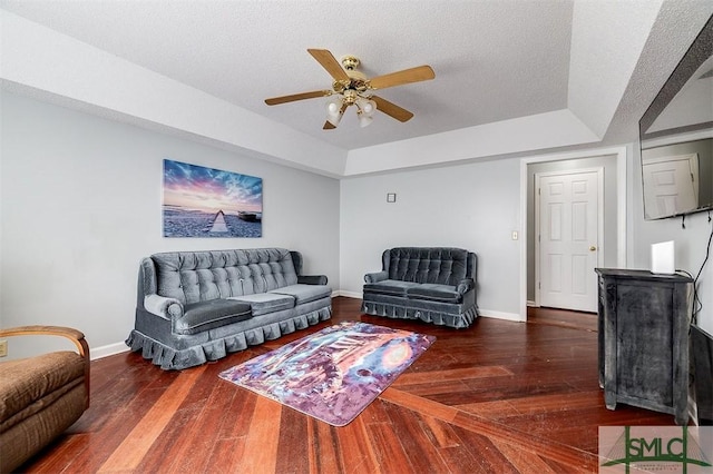 living room with a textured ceiling, a raised ceiling, ceiling fan, and dark wood-type flooring