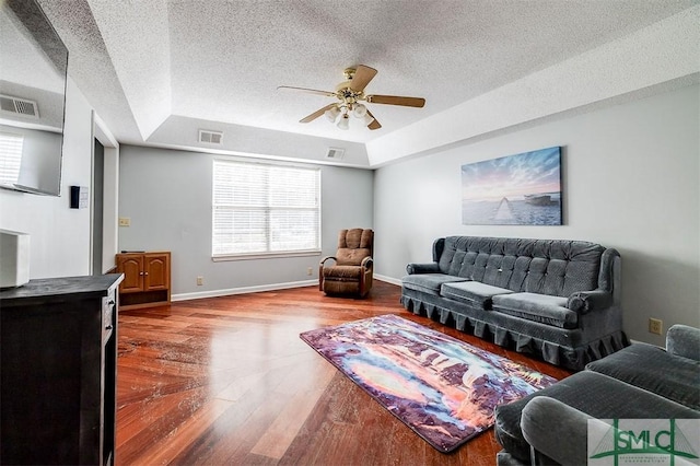 living room with ceiling fan, a raised ceiling, wood-type flooring, and a textured ceiling