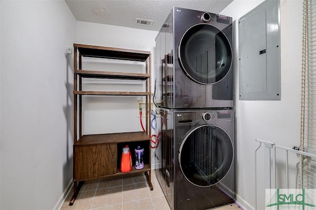 laundry area with light tile patterned floors, a textured ceiling, electric panel, and stacked washer and clothes dryer