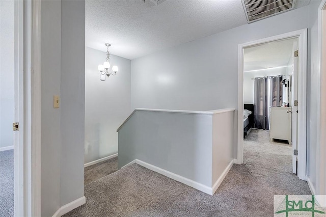 hallway with light carpet, a textured ceiling, and a notable chandelier