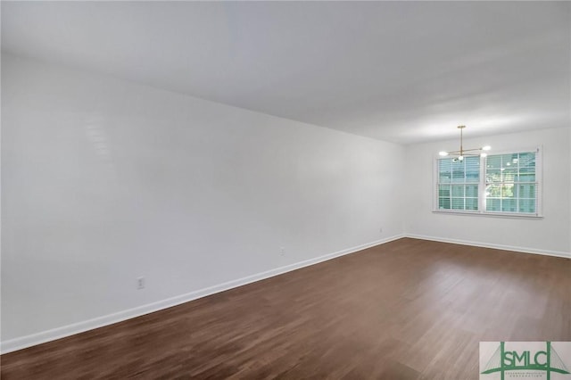 empty room with dark hardwood / wood-style flooring and a notable chandelier