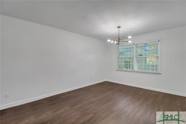 spare room featuring dark wood-type flooring and a chandelier