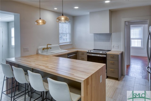 kitchen featuring kitchen peninsula, stainless steel appliances, decorative light fixtures, a breakfast bar area, and butcher block counters