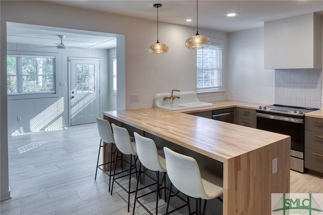 kitchen with ceiling fan, hanging light fixtures, a kitchen breakfast bar, wooden counters, and appliances with stainless steel finishes