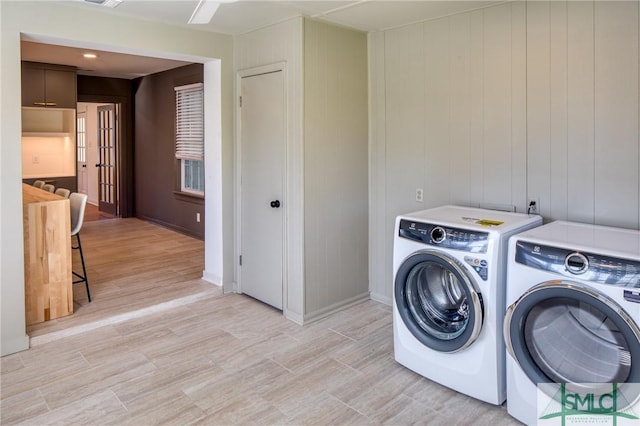 clothes washing area featuring washing machine and clothes dryer, wooden walls, and light hardwood / wood-style flooring