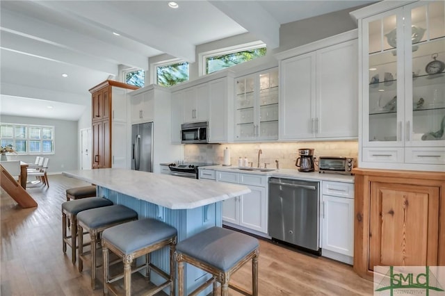 kitchen featuring decorative backsplash, stainless steel appliances, sink, beamed ceiling, and white cabinetry