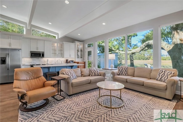 living room featuring lofted ceiling with beams, light hardwood / wood-style flooring, a healthy amount of sunlight, and sink