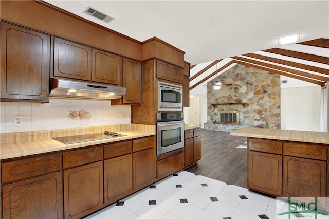 kitchen with appliances with stainless steel finishes, tasteful backsplash, lofted ceiling with beams, a fireplace, and butcher block counters