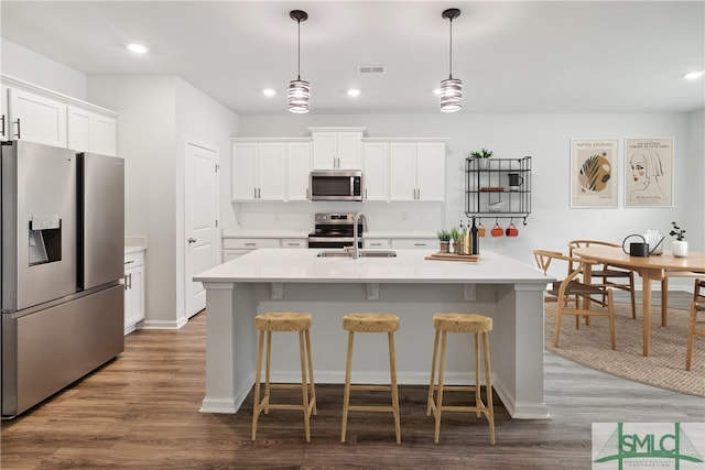 kitchen with a center island with sink, sink, hanging light fixtures, white cabinetry, and stainless steel appliances