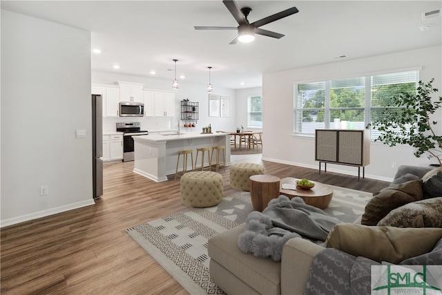 living room featuring ceiling fan, sink, and light wood-type flooring