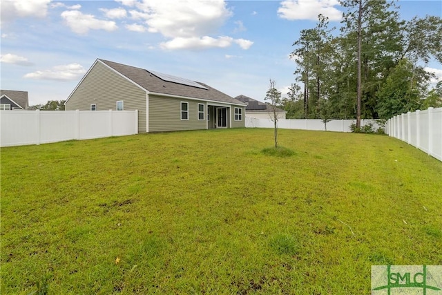 rear view of property featuring a lawn and solar panels