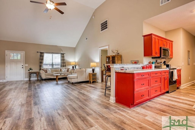 kitchen with ceiling fan, light hardwood / wood-style floors, a breakfast bar area, high vaulted ceiling, and appliances with stainless steel finishes