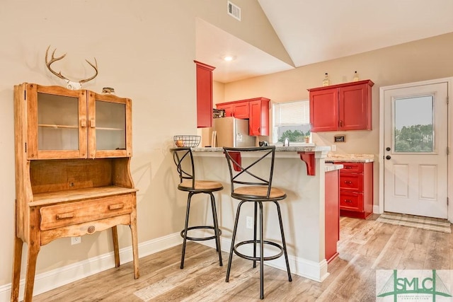 kitchen with stainless steel refrigerator, kitchen peninsula, light hardwood / wood-style floors, and lofted ceiling