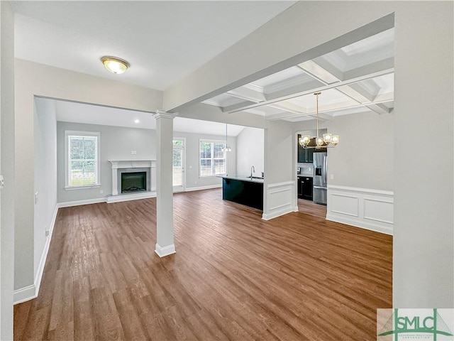 unfurnished living room with sink, dark wood-type flooring, coffered ceiling, beamed ceiling, and a notable chandelier