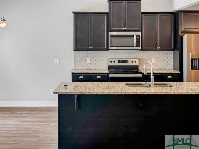 kitchen featuring light stone countertops, appliances with stainless steel finishes, backsplash, dark brown cabinetry, and sink