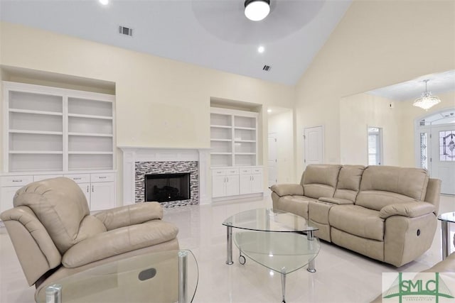 living room with a tile fireplace, built in features, ceiling fan with notable chandelier, and lofted ceiling