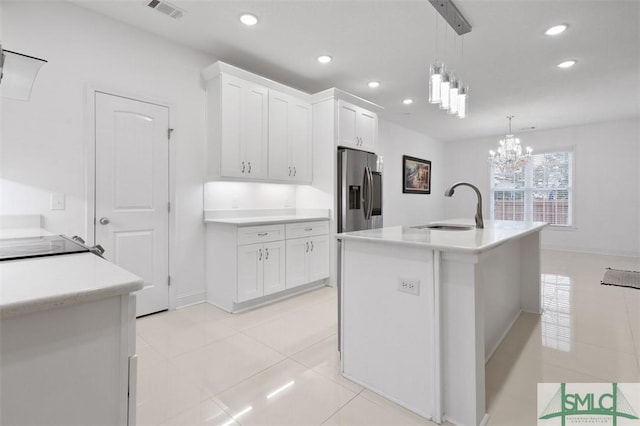 kitchen with sink, stainless steel refrigerator with ice dispenser, pendant lighting, a center island with sink, and white cabinets