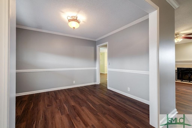 spare room with ceiling fan, dark hardwood / wood-style flooring, crown molding, a textured ceiling, and a fireplace