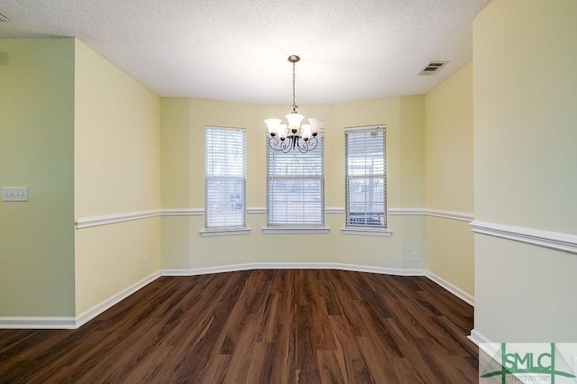 unfurnished dining area with dark hardwood / wood-style floors, a textured ceiling, and a chandelier