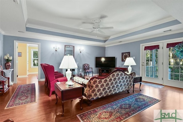 living room featuring a raised ceiling, ornamental molding, ceiling fan, and a wealth of natural light