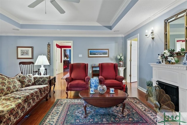 living room featuring ceiling fan, dark hardwood / wood-style flooring, ornamental molding, and a tray ceiling