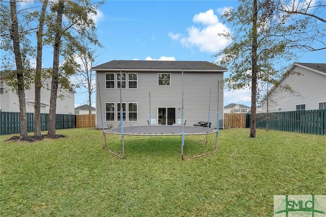 rear view of property with a trampoline and a yard