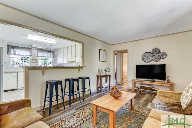 living room featuring light wood-type flooring, a wall unit AC, and crown molding