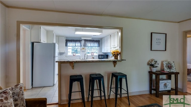 kitchen with kitchen peninsula, a kitchen breakfast bar, light stone countertops, white fridge, and white cabinetry