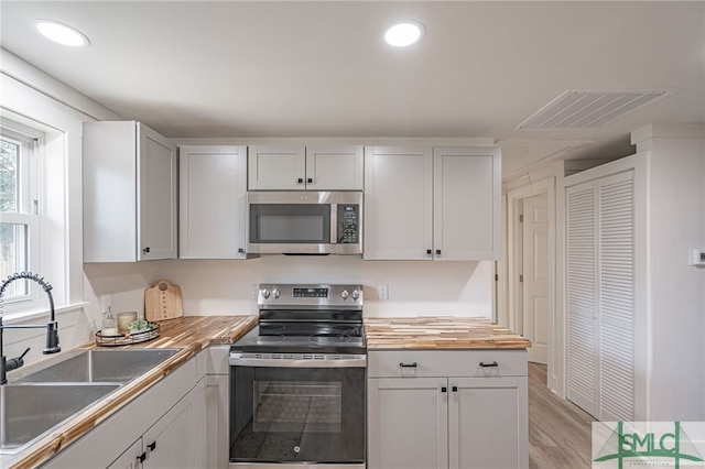 kitchen with butcher block countertops, light hardwood / wood-style floors, sink, and appliances with stainless steel finishes